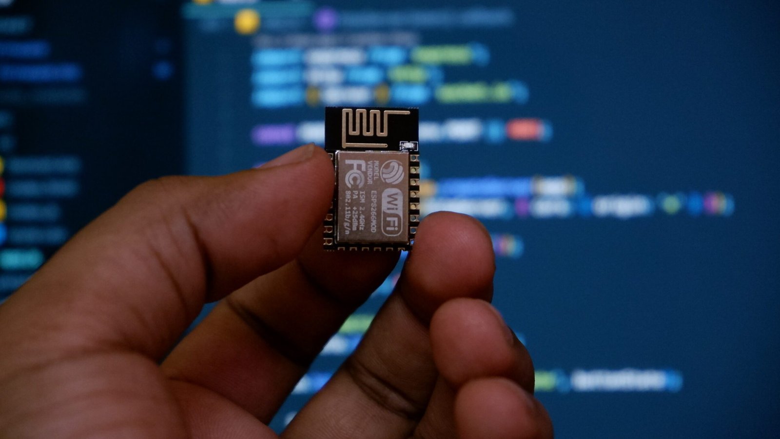 a hand holding a micro processor chip in front of a computer screen